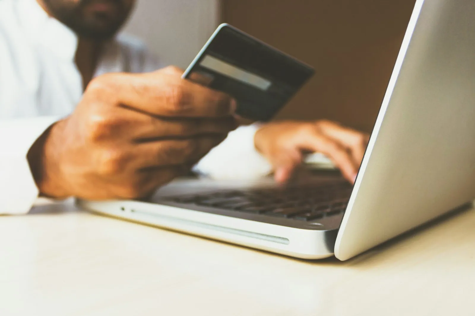 Hand holding a bank card over a laptop keyboard at an online checkout